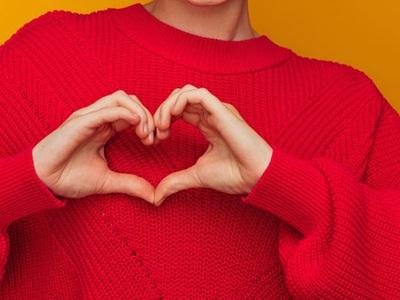 A woman in a red sweater makes a heart with her hands