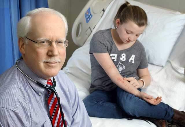 Dr. Robert Wood in a hospital room with his pediatric allergy patient as she looks at the allergy test on her arm
